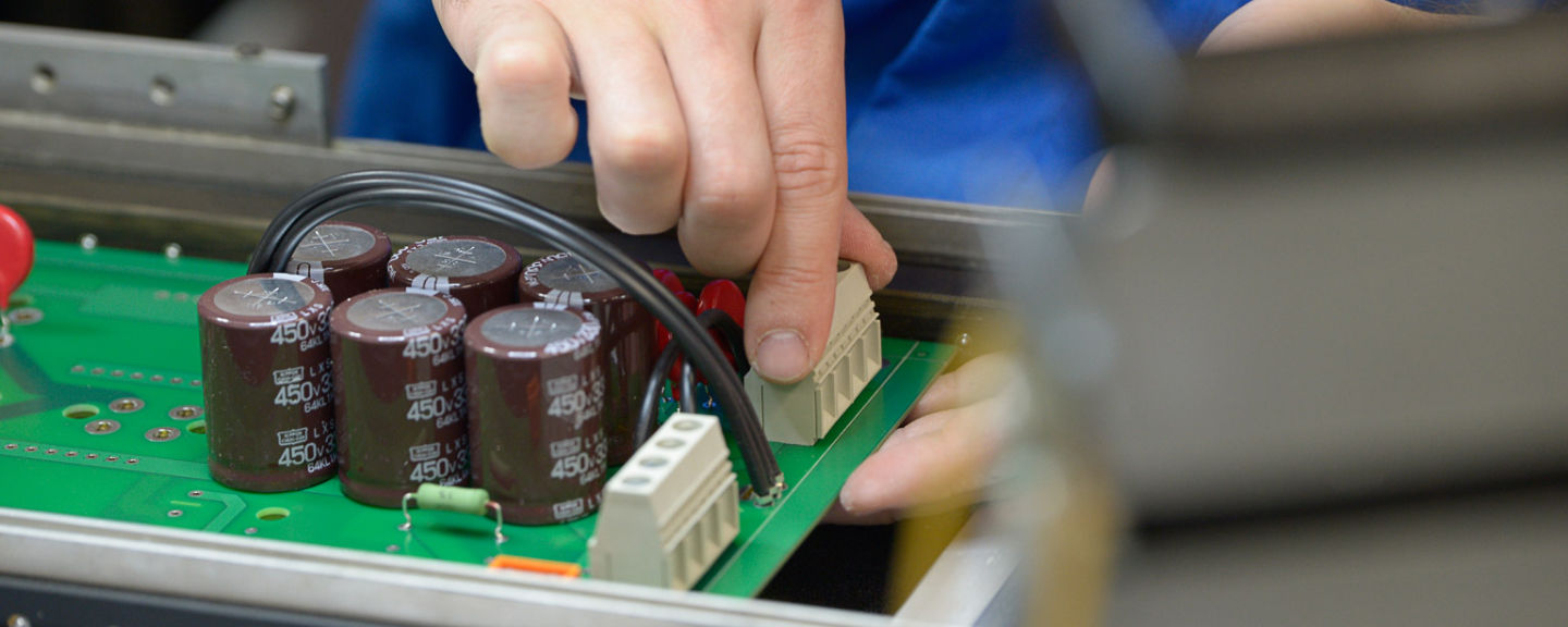 Eine Leiterplatte wird mit elektronischen Bauteilen von Hand bestückt.